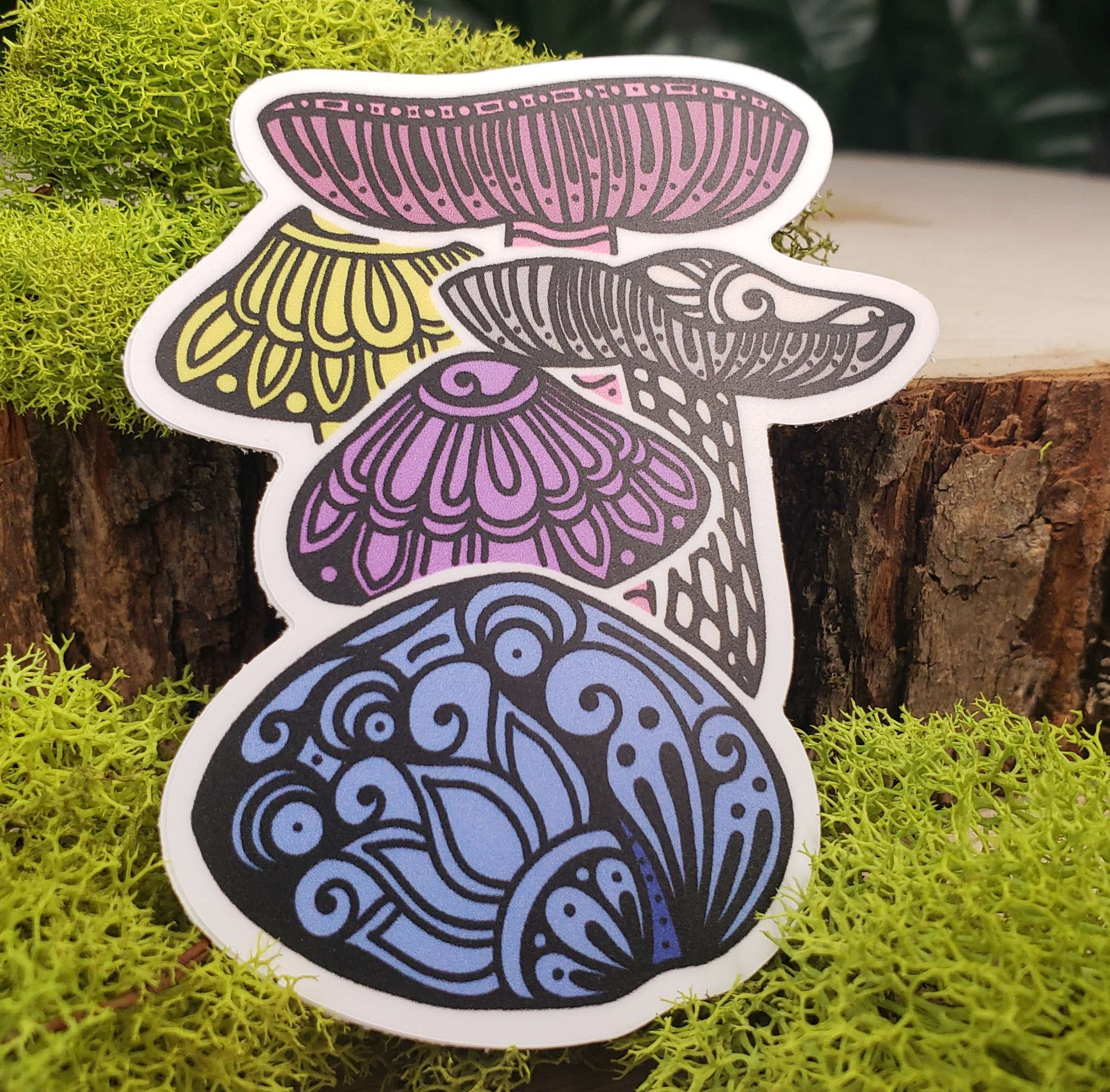 Sticker of pastel pink, yellow, purple, blue, and cream crimson wax cap mushrooms with stark black line art reminiscent of henna tattoo art. the sticker is sitting on moss and wood with ivy leaves in the background