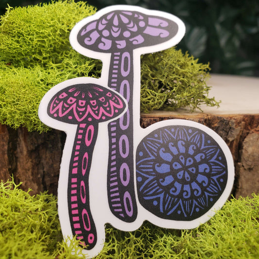 Sticker of purple, pink, and blue amethyst deceiver mushrooms with stark black line art reminiscent of henna tattoo art. the sticker is sitting on moss and wood with ivy leaves in the background