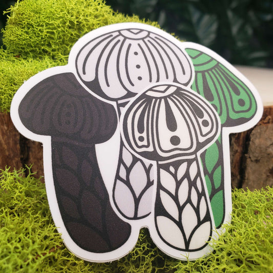 Sticker of green, cream, pale gray, and black wine cap mushrooms with stark black line art reminiscent of henna tattoo art. the sticker is sitting on moss and wood with ivy leaves in the background