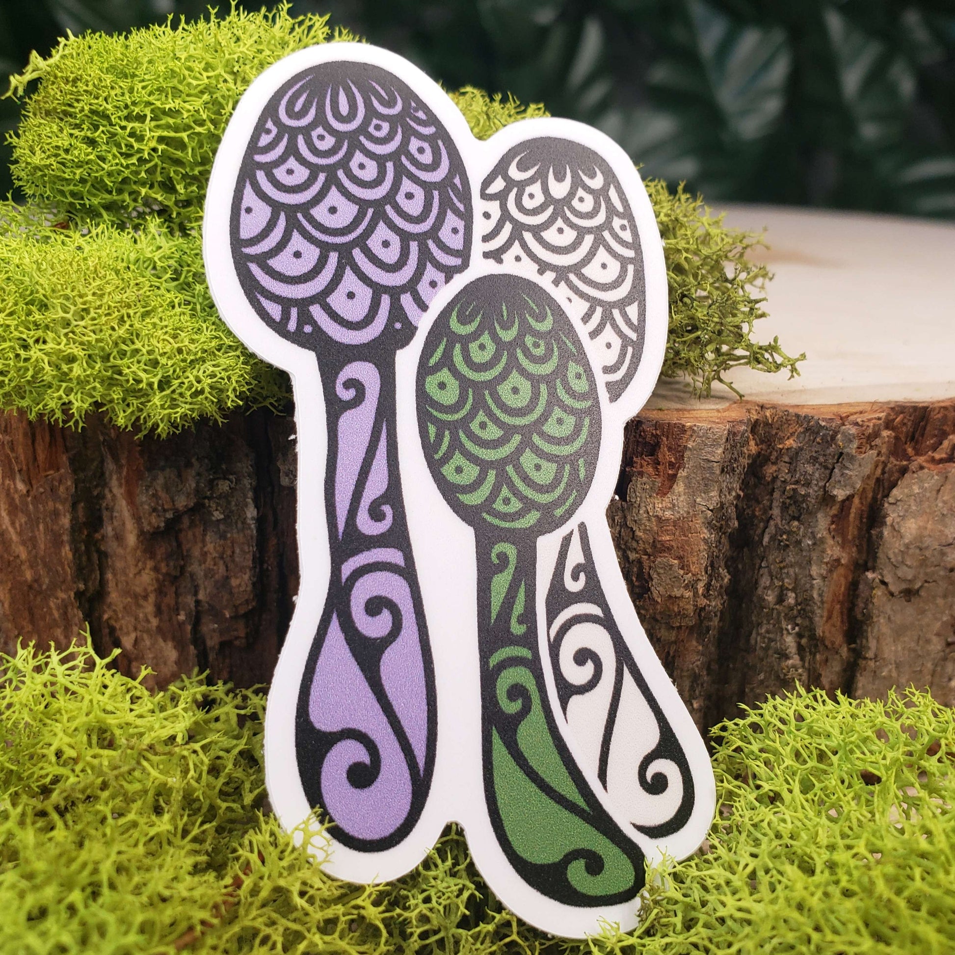 Sticker of green, purple, and cream flowerpot parasol mushrooms with stark black line art reminiscent of henna tattoo art. the sticker is sitting on moss and wood with ivy leaves in the background