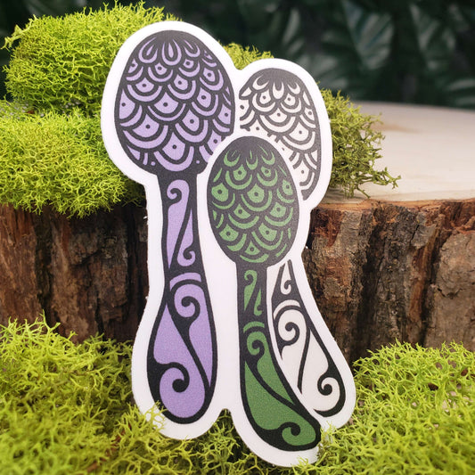 Sticker of green, purple, and cream flowerpot parasol mushrooms with stark black line art reminiscent of henna tattoo art. the sticker is sitting on moss and wood with ivy leaves in the background