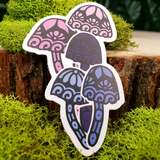 Sticker of pastel pink, medium pink, pastel blue, medium blue, and dark blue mica cap mushrooms with stark black line art reminiscent of henna tattoo art. the sticker is sitting on moss and wood with ivy leaves in the background